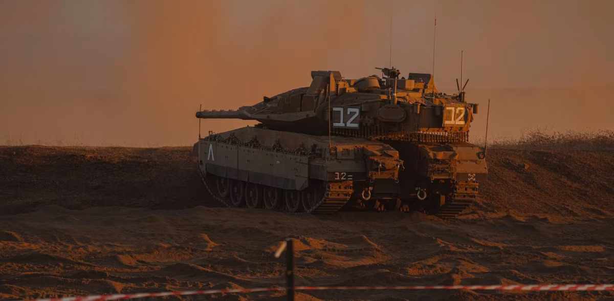 Merkava Mark 5 tank numbered "12" positioned on a sandy berm at dusk, turret facing left