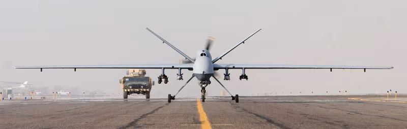 An MQ-9 Reaper unmanned aerial vehicle taxis down a runway at Kandahar Airfield, Afghanistan, with a military Humvee visible in the background, October 2007