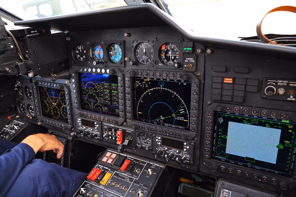 Ka-52 Alligator cockpit interior showing multifunction displays, analog gauges, and the side-by-side instrument panel layout with a crew member's hand visible on the controls