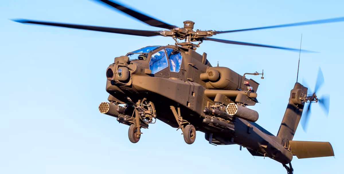 An AH-64 Apache in flight, showing its M230 chain gun, Hydra rocket pods, Hellfire missile launchers, and TADS sensor ball mounted under the nose.