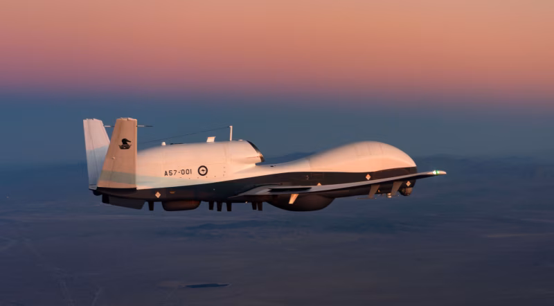 Northrop Grumman MQ-4C Triton high-altitude maritime surveillance drone flying at sunset over ocean terrain