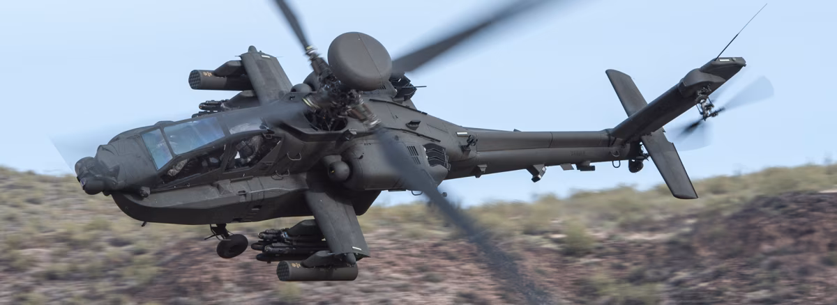 An AH-64D Apache Longbow flying low over desert terrain, with the AN/APG-78 Longbow radar dome clearly visible above the rotor hub.